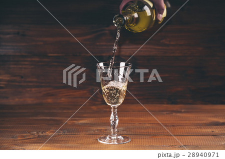 Pouring white wine from a bottle in a wineglasses  28940971