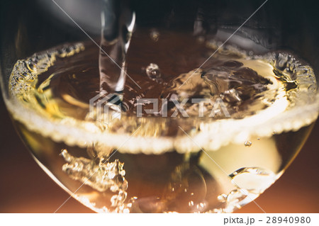 Pouring white wine from a bottle in a wineglasses 28940980