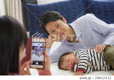 パパと赤ちゃんの寝顔をスマホ撮影するママ 29012312