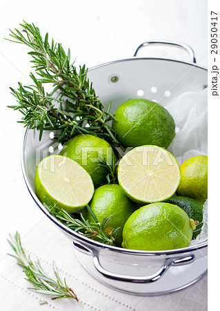 Fresh limes and rosemary in white enamel colander. 29050417