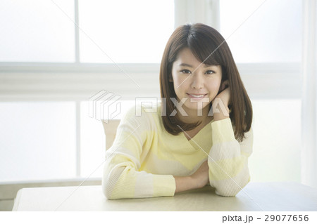 テーブルで頬杖をする笑顔の20代女性 29077656