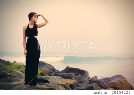 beautiful young woman standing on the stone coast 29154225