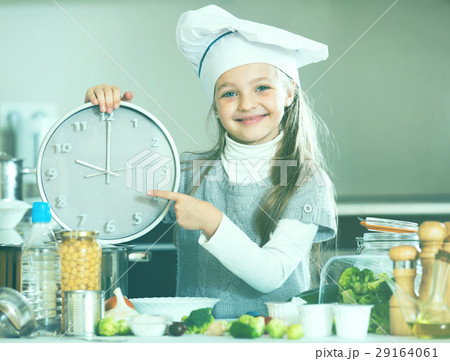Girl in cook cap holding clock at domestic kitchen Girl in cook cap holding clock at domestic kitchen 29164061