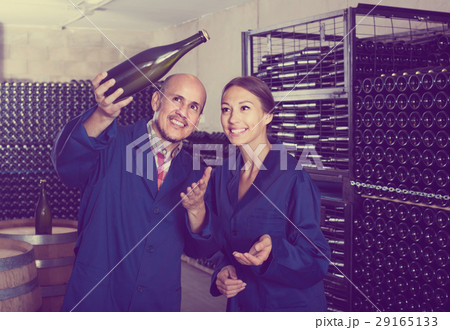 man and women coworkers looking at bubbly wine in bottle standing in wine cellar 29165133