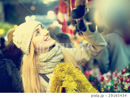Smiling young woman choosing Christmas decoration at market Smiling young woman choosing Christmas decoration at market 29165434