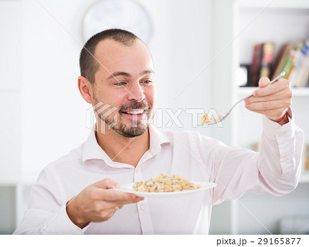 Positive young man eating porridge Positive young man eating porridge 29165877