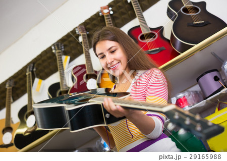 Teenage girl selecting guitar in shop. 29165988
