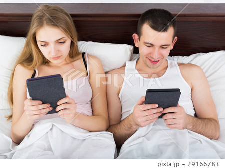 Young couple reading news from e-readers in bed 29166783