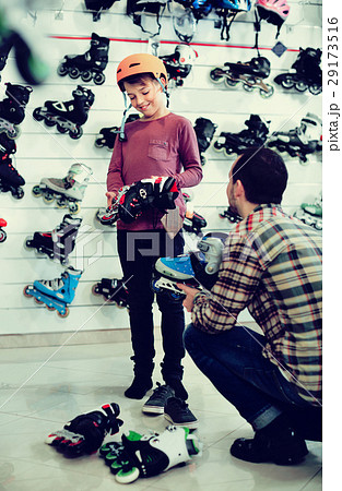 Man seller assisting boy in trying on roller-skates Man seller assisting boy in trying on roller-skates 29173516