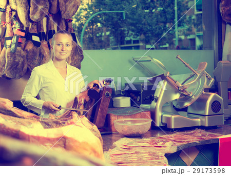 Woman in uniform slicing delicious prosciutto meat 29173598