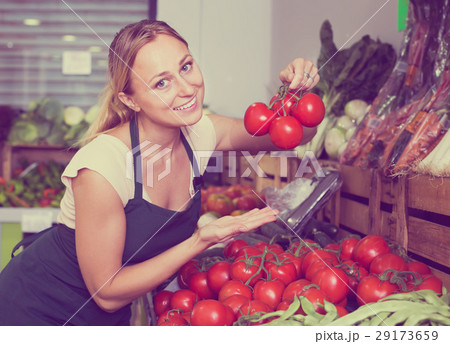 Glad young female seller holding fresh ripe tomatoes on market 29173659
