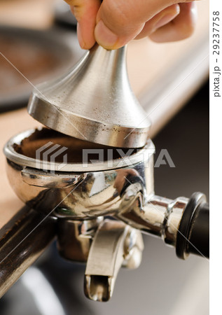 Barista pressing ground coffee into portafilter 29237758