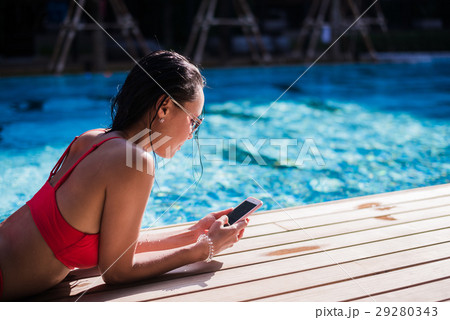 Beautiful woman leaning on poolside and typing a 29280343