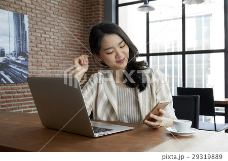 The young lady is using her smarphone, sitting in front of the laptop The young lady is using her smarphone, sitting in front of the laptop 29319889