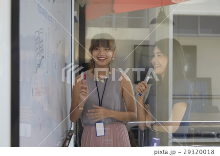 female colleagues standing near whiteboard and discussing some new ideas together. 29320018