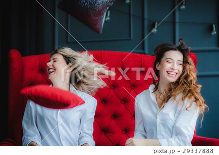 2 happy models have fight with pillows on red sofa 2 happy models have fight with pillows on red sofa 29337888
