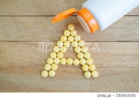 Yellow pills forming shape to A alphabet on wood 29361030