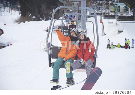 スキー場 リフトに乗るカップル スマホ 撮影の写真素材