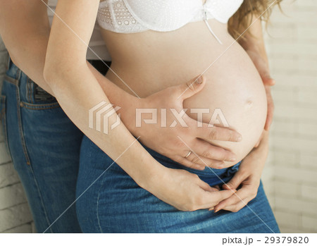 A pregnant woman with her husband hugging his arms 29379820