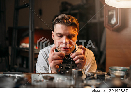 Watchmaker holding with tweezers a gear of hours 29442387