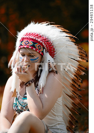 Young woman in war bonnet headdress of American Indian smokes a pipe Young woman in war bonnet headdress of American Indian smokes a pipe 29465138
