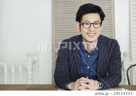 机の前で手を組む笑顔の30代男性 29553333