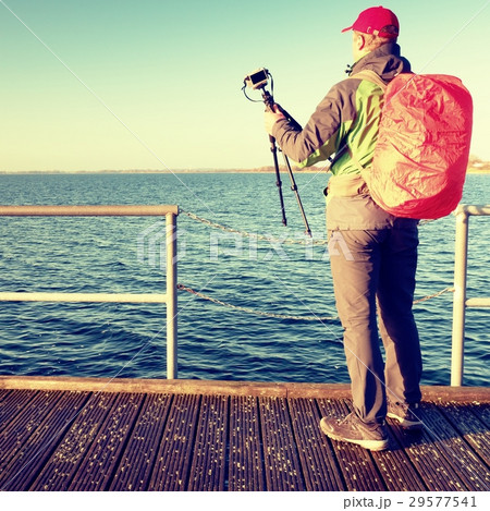 Photographer with red backpack on pier at sea Photographer with red backpack on pier at sea 29577541