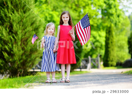 Two adorable little sisters holding american flags outdoors on beautiful summer day Two adorable little sisters holding american flags outdoors on beautiful summer day 29633000