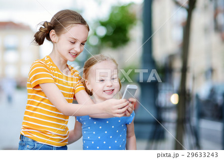Two cute little sisters playing outdoor mobile game on their smart phones 29633243