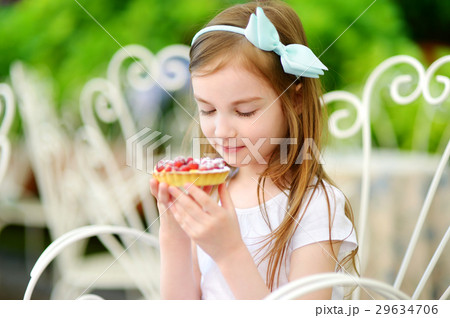 Adorable little girl eating fresh sweet strawberry cake outdoors on warm and sunny summer day Adorable little girl eating fresh sweet strawberry cake outdoors on warm and sunny summer day 29634706