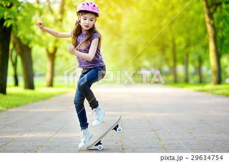 Pretty little girl learning to skateboard outdoors 29634754