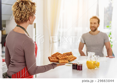 Cheerful housewife serving waffles on table Cheerful housewife serving waffles on table 29663844