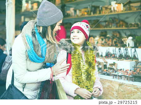 Female customers staring at counter of kiosk with figures for creating miniature Christmas scenes 29725215