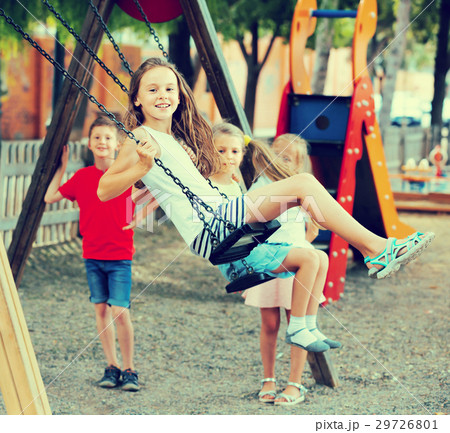 Smiling girls and boys swinging on playground 29726801