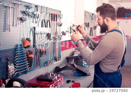 Young man is observing motorbike part for fixing Young man is observing motorbike part for fixing 29727080