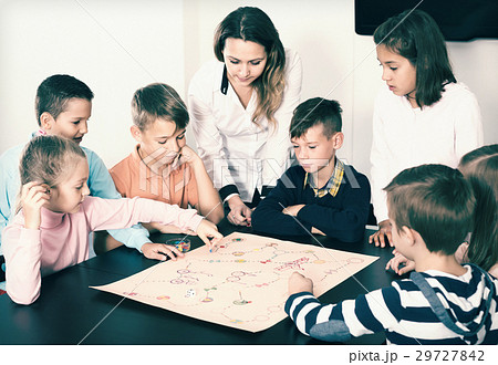 Teacher and happy kids sitting at table with board game 29727842