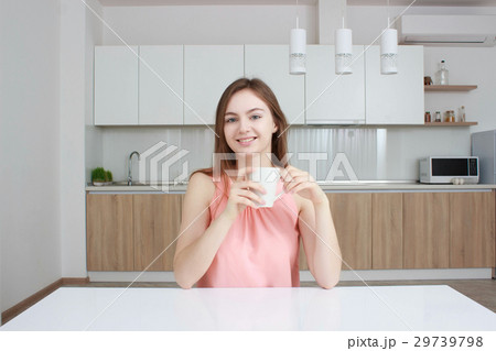 Smiling woman which sitting on kitchen with cup of Smiling woman which sitting on kitchen with cup of 29739798