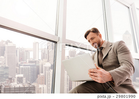 Low angle of serious businessman using laptop 29801990