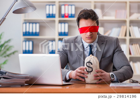 Blindfold businessman sitting at desk in office Blindfold businessman sitting at desk in office 29814196