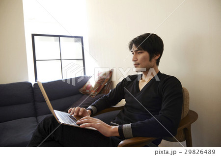 リビングルームの椅子に座ってパソコンを使う男性。 29826489