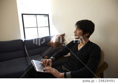 リビングルームの椅子に座ってパソコンを使う男性。 29826491