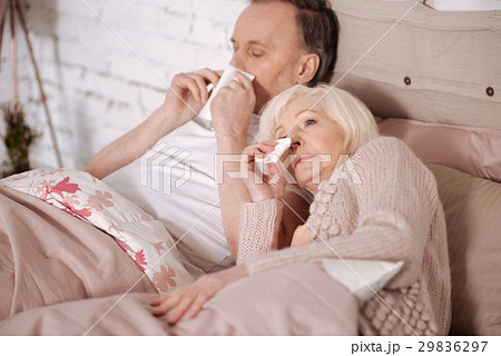 Senior couple blowing noses on bed 29836297