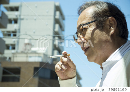 ベランダでタバコを吸うシニア男性の写真素材