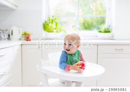 Baby boy eating apple in white kitchen at home 29965081