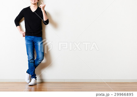 部屋の壁の前に立っている男性,ジーンズ 29966895