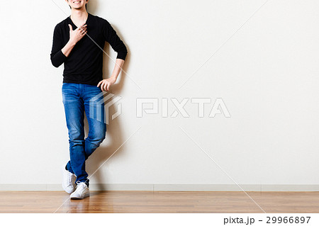 部屋の壁の前に立っている男性,ジーンズ 29966897