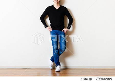 部屋の壁の前に立っている男性,ジーンズ 29966909