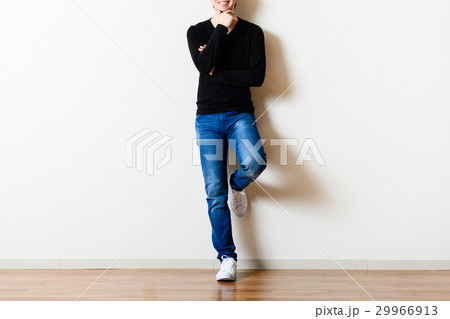 部屋の壁の前に立っている男性,ジーンズ 29966913
