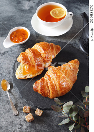 Two fresh croissants, jam, lemon tea and teapot 29998870