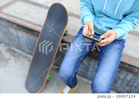 young skateboarder use cellphone  at skatepark 30007324